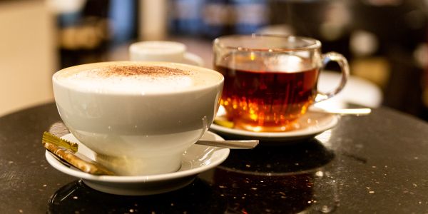 Großer Cappuccino mit deftiger Milchhaube und ein heißer, klarer Tee zum Verzehren bereit