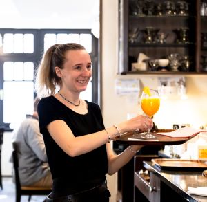 Mitarbeiterin mit einem Glas Orangensaft beim Kellnern
