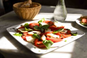 Quadratischer Teller mit Tomate-Mozzarella-Salat, garniert mit frischen Basilikumblättern und Balsamico-Creme.