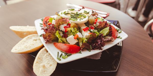 Reichhaltiger Salat mit Feta-Käse, Ei, Tomaten, Oliven und Schnittlauch. Baguette als Beilage.