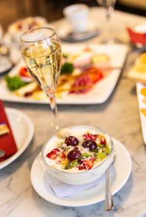 Gedeckter Frühstückstisch mit elegant dekorierter Käse-Wurst-Platte, prikelndem Sekt und frischen Früchten auf Joghurt