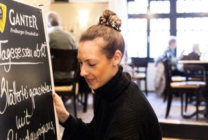 Mitarbeiterin trägt die Tafel mit Tagesessenangeboten