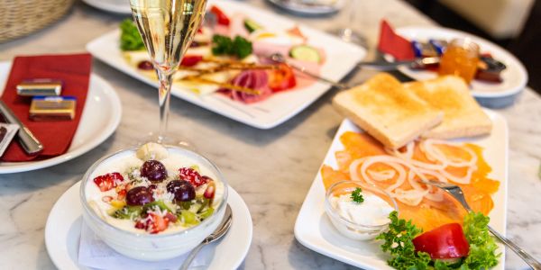 Gedeckter Frühstückstisch mit Räucherlachs, elegant dekorierter Käse-Wurst-Platte, prikelndem Sekt und frischen Früchten auf Joghurt