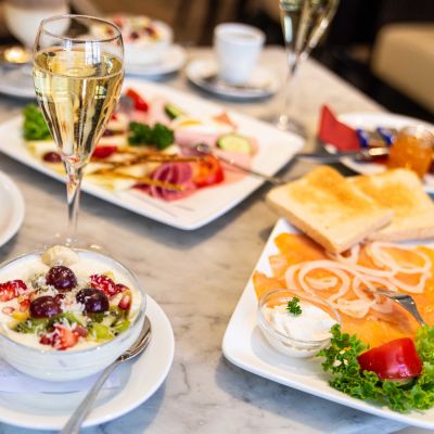 Gedeckter Frühstückstisch mit Räucherlachs, elegant dekorierter Käse-Wurst-Platte, prikelndem Sekt und frischen Früchten auf Joghurt