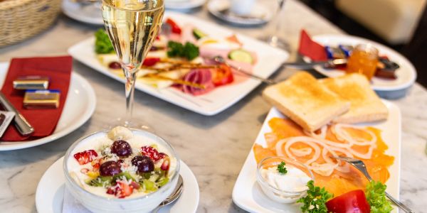 Gedeckter Frühstückstisch mit Räucherlachs, elegant dekorierter Käse-Wurst-Platte, prikelndem Sekt und frischen Früchten auf Joghurt