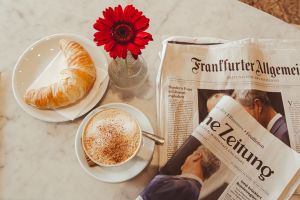 Kaffe, Crosaint, eine rote Blume, und Zeitungen auf einem Marmortisch