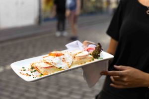 Servierplatte mit zwei mit Käse überbackenen Toasts und Spiegeleiern, von einer Person getragen.