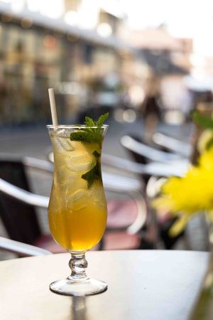 Eistee-Cocktail im Tulpenglas mit Eiswürfeln, frischer Minze und Trinkhalm auf einem Tisch im Außenbereich.