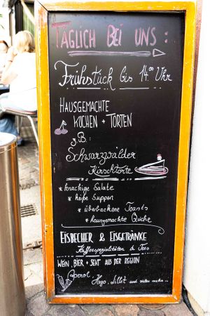 Beschriebene Kreidetafel im Holzrahmen mit Angeboten zu Frühstück, Kuchen, Eisspezialitäten und Getränken.