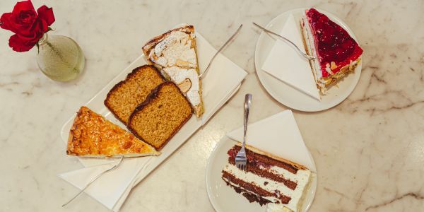 Verschiedene Kuchenstücke auf einem weißen Marmortisch mit roter Rose, serviert auf Tellern mit Servietten und in die Kuchen gesteckten Gabeln