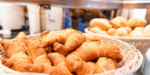 Geflochtener Weidenkorb gefüllt mit frischen Croissants, im Hintergrund ein Korb mit Brötchen.