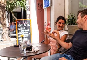 Fröhliches Paar sitzt im Café-Außenbereich und stößt an mit fruchtigen Sommergetränken