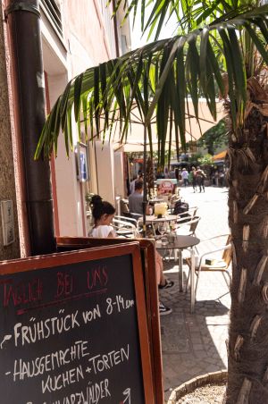 Lebhafter Café-Außenbereich neben einer Fußgängerzone mit spazierenden Passanten
