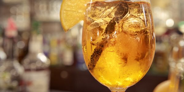 Gelber Cocktail mit Eiswürfeln, Strohhalm und einer Zitrusscheibe