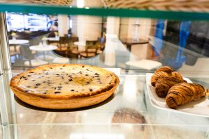 Glasvitrine mit einem Blaubeerkuchen und drei mit Schokolade verzierten Croissants auf einem Teller.